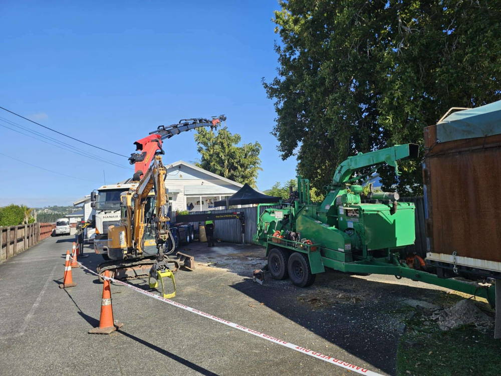 Hiab truck, mini excavator and chipper working behind road cones and tape outside a Whangarei house
